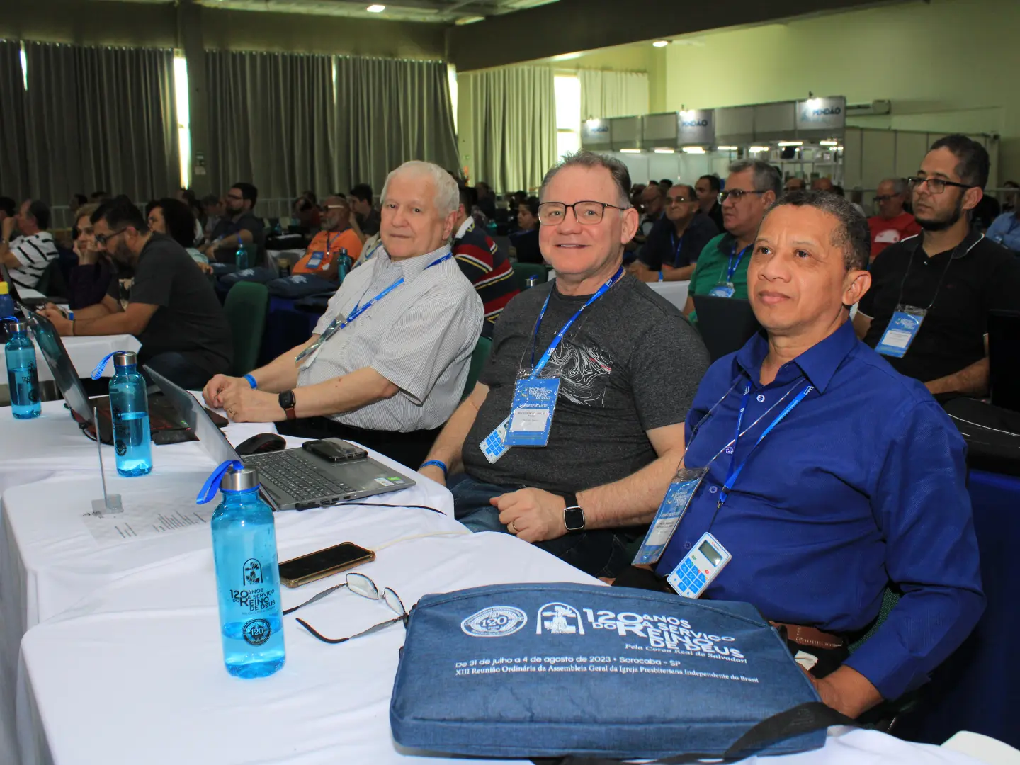 Rev. Gerson sentado à mesa de trabalho da Assembleia Geral, entre outros representantes